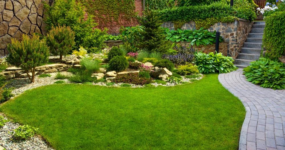 Jardin paysager avec pelouse impeccable, massifs de vivaces et arbustes ornementaux, allée en pavés courbes, escalier en pierre naturelle et murs de soutènement en brique et pierre