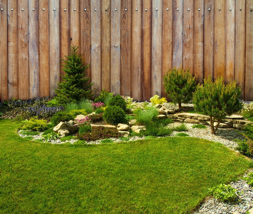 Terrasse extérieure aménagée avec salon de jardin en bois, jardin paysager en arrière-plan, bordures végétalisées et pots de fleurs colorées